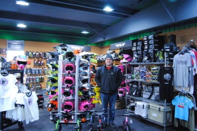 Owner of Go Fasters posing in his store with snowmobile helmets in the background.