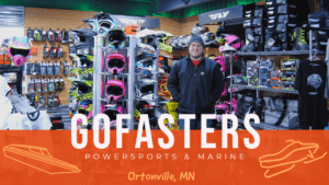 Owner of Go Fasters posing in his store with snowmobile helmets in the backgrounnd.