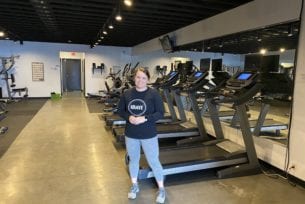 Owner of Krave Wellness posing in her gym with teadmilles, bikes, and elipticals in the bakcground.